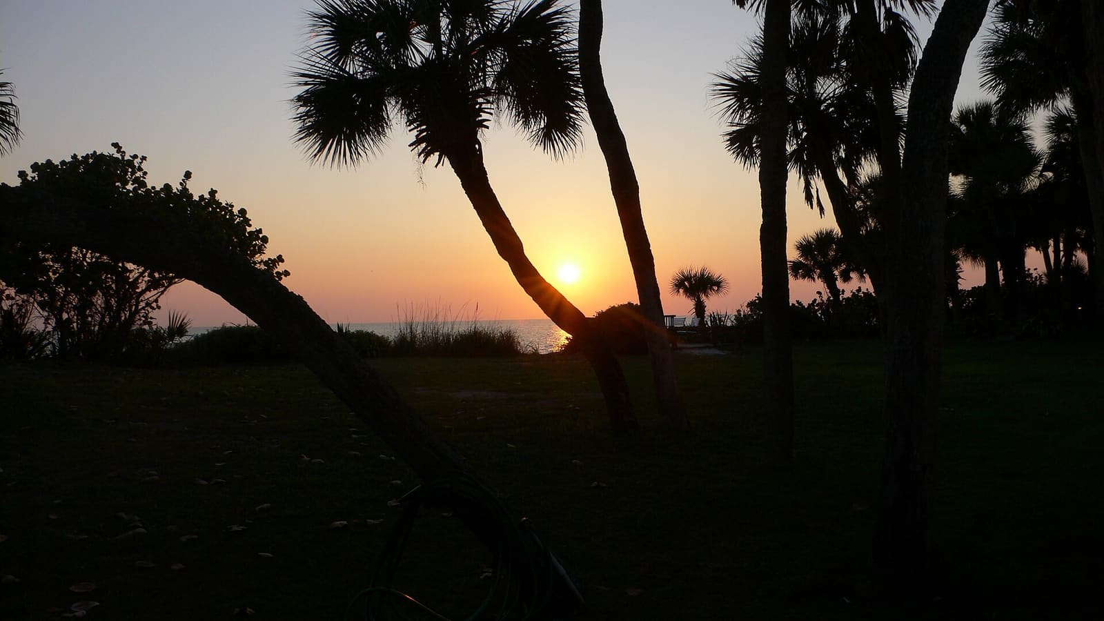 Florida: The sun sets over the Gulf of Mexico, its reflection shining in the ocean water. Silhouetted against the sky are shadowy